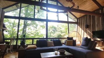Un intérieur de chalet chaleureux avec une grande fenêtre, des meubles en bois et un téléviseur.