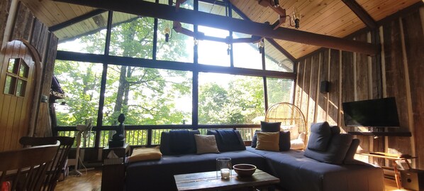 Interior acogedor de una cabaña con un ventanal grande, muebles de madera y un televisor.