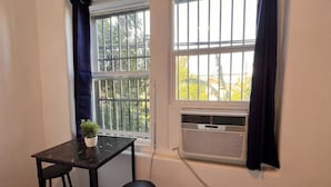 Quarto com duas janelas, uma mesa e duas cadeiras, e um aparelho de ar condicionado.