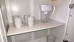 Um armário de cozinha com canecas brancas, uma cafeteira e pratos empilhados.