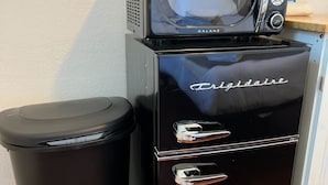 Cozinha compacta com geladeira, micro-ondas e lixeira.