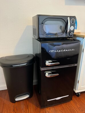 Eine kompakte Küchenzeile mit Kühlschrank, Mikrowelle und Mülleimer.