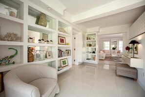 A spacious living area with a large white sofa, a bookshelf filled with various items, and a coffee table. - Historic Estate with Private Pool, Golf Cart, Walk to Town and Beach (Governor's Harbour)