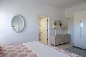 A bedroom with a bed, a dresser, a mirror, and a door leading to a bathroom. - Historic Estate with Private Pool, Golf Cart, Walk to Town and Beach (Governor's Harbour)
