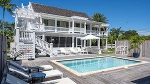 Ein zweistöckiges Haus mit Pool, Gartenmöbeln und einer Holzterrasse.