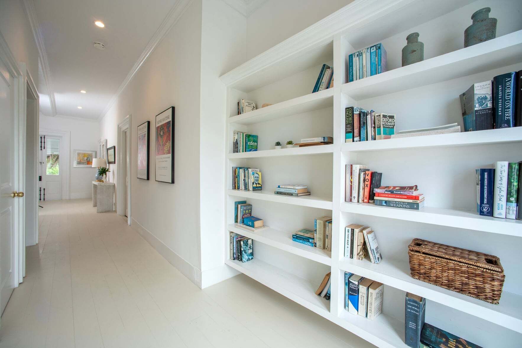 Un couloir avec une bibliothèque blanche remplie de livres et d’objets décoratifs.