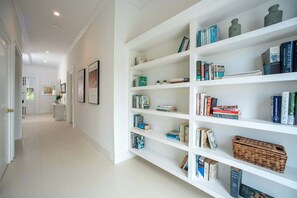 A hallway with a white bookshelf filled with books and decorative items. - Historic Estate with Private Pool, Golf Cart, Walk to Town and Beach (Governor's Harbour)