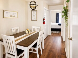 Ein Essbereich mit Holztisch und weißen Stühlen, ein Schild mit der Aufschrift 'Küche' und ein Gang zum Schlafzimmer.