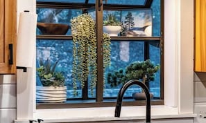 Une fenêtre donnant sur un paysage enneigé, une plante suspendue et une plante en pot posée sur le rebord de la fenêtre.