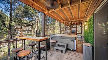 A wooden deck with a bar area, seating, and a view of the forest.