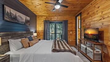 A wooden cabin bedroom with a bed, a ceiling fan, a TV, and a window.