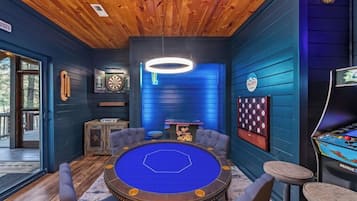 A room with a pool table, dartboard, and pinball machine.