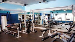 Ein Fitnessstudio mit verschiedenen Trainingsgeräten, darunter Kurzhanteln, Kraftgeräte und ein Laufband.