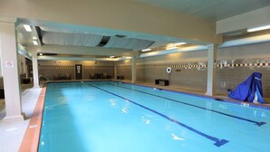 Ein großes Hallenbad mit deutlichen Fahrbahnmarkierungen, einer gefliesten Wand und einem überdachten Bereich auf der rechten Seite.