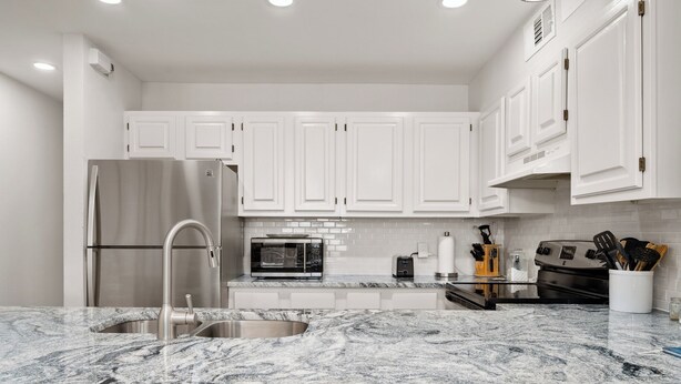 Une cuisine moderne avec des meubles blancs, un réfrigérateur en acier inoxydable, un four à micro-ondes et une cuisinière.