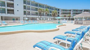 Une piscine avec des chaises longues, un immeuble à plusieurs étages doté de balcons et une zone aménagée en plage.