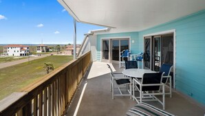 Un balcon avec vue sur la plage, une table avec des chaises et une porte-fenêtre coulissante.