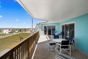 Ein Balkon mit Blick auf den Strand, ein Tisch mit Stühlen und eine Glastür.
