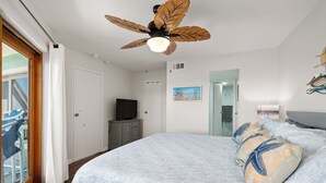Une chambre à coucher avec un lit, un ventilateur de plafond, une télévision et des œuvres d’art accrochées au mur.