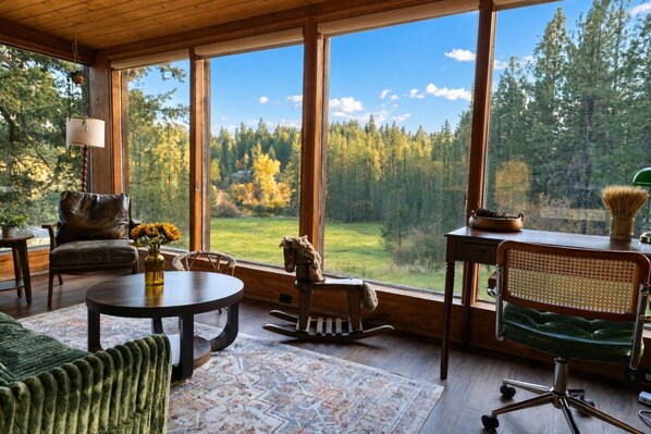 A spacious room with large windows, a leather chair, a dining table, and a green sofa.