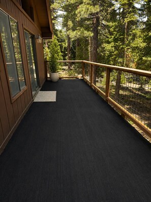 A wooden deck with a black rubber mat, a potted plant, and a metal railing.