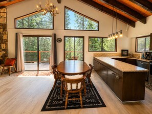 A spacious kitchen with a large island, wooden dining table, and multiple windows offering views of the outdoors.