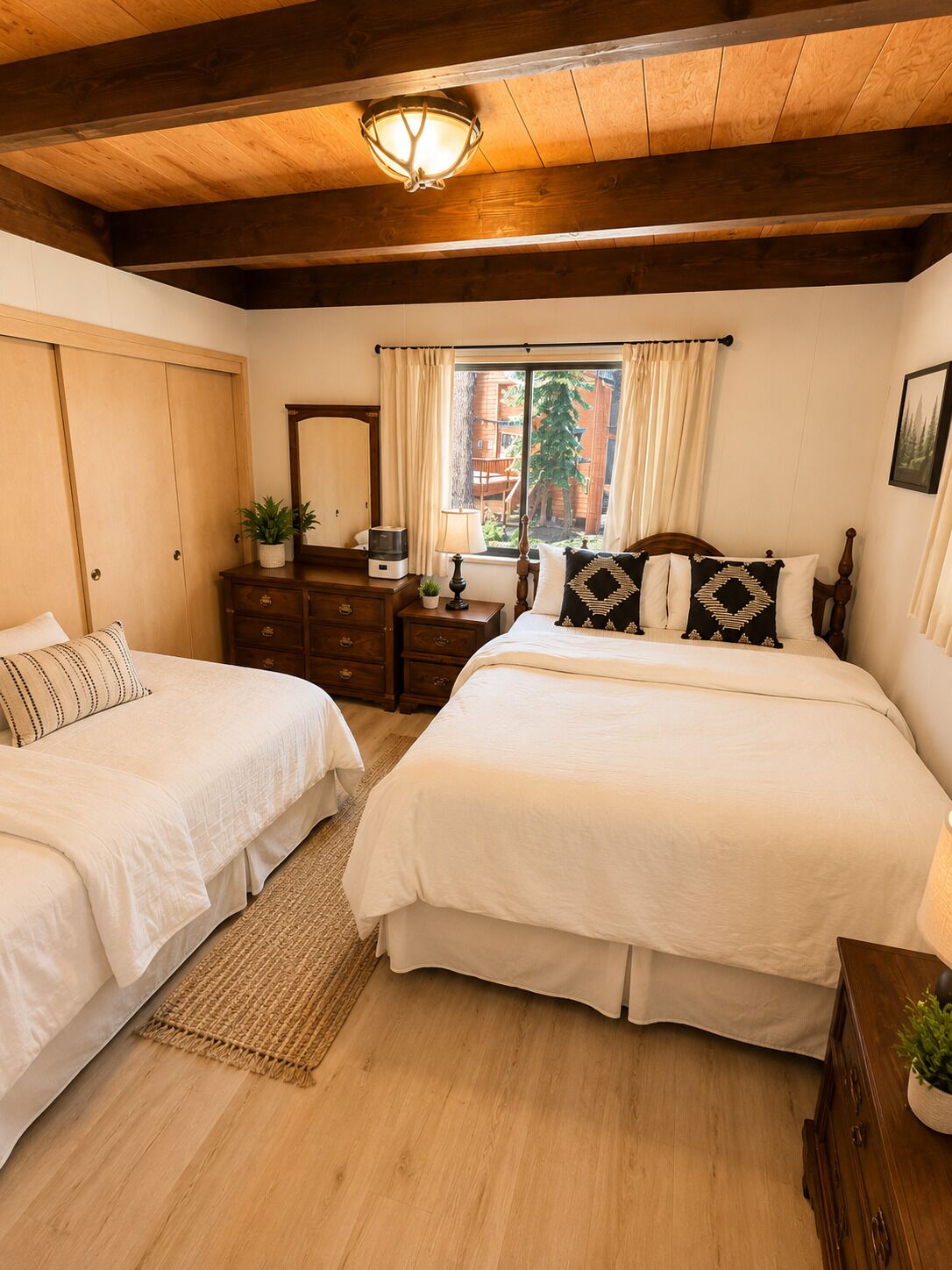 Un dormitorio con dos camas, vigas de madera en el techo, una ventana con cortinas, un aparador y un espejo.