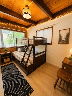 A bedroom with a bunk bed, a desk, a chair, a lamp, and a window with blinds.