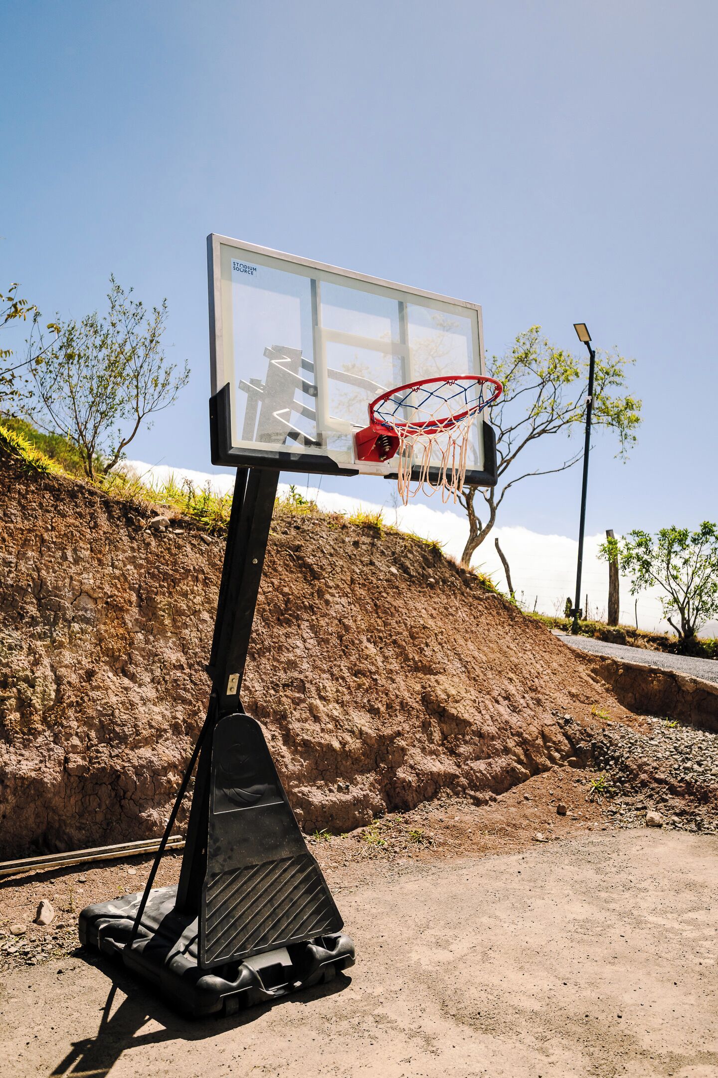 A basketball hoop with a clear view of the backboard and net, set against a hilly landscape with sparse vegetation.