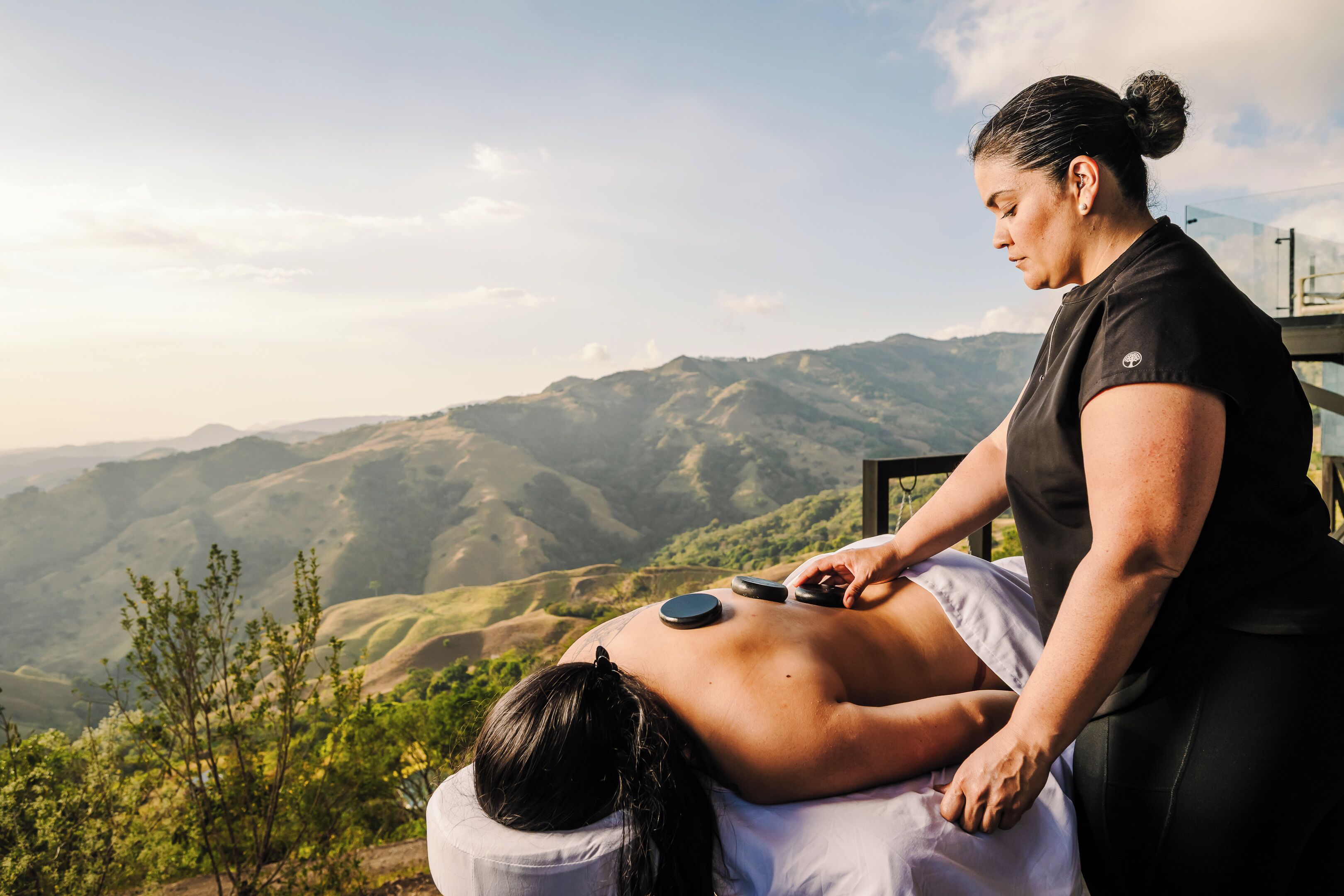 Eine Person erhält eine Rückenmassage im Freien, mit einer Berglandschaft im Hintergrund.