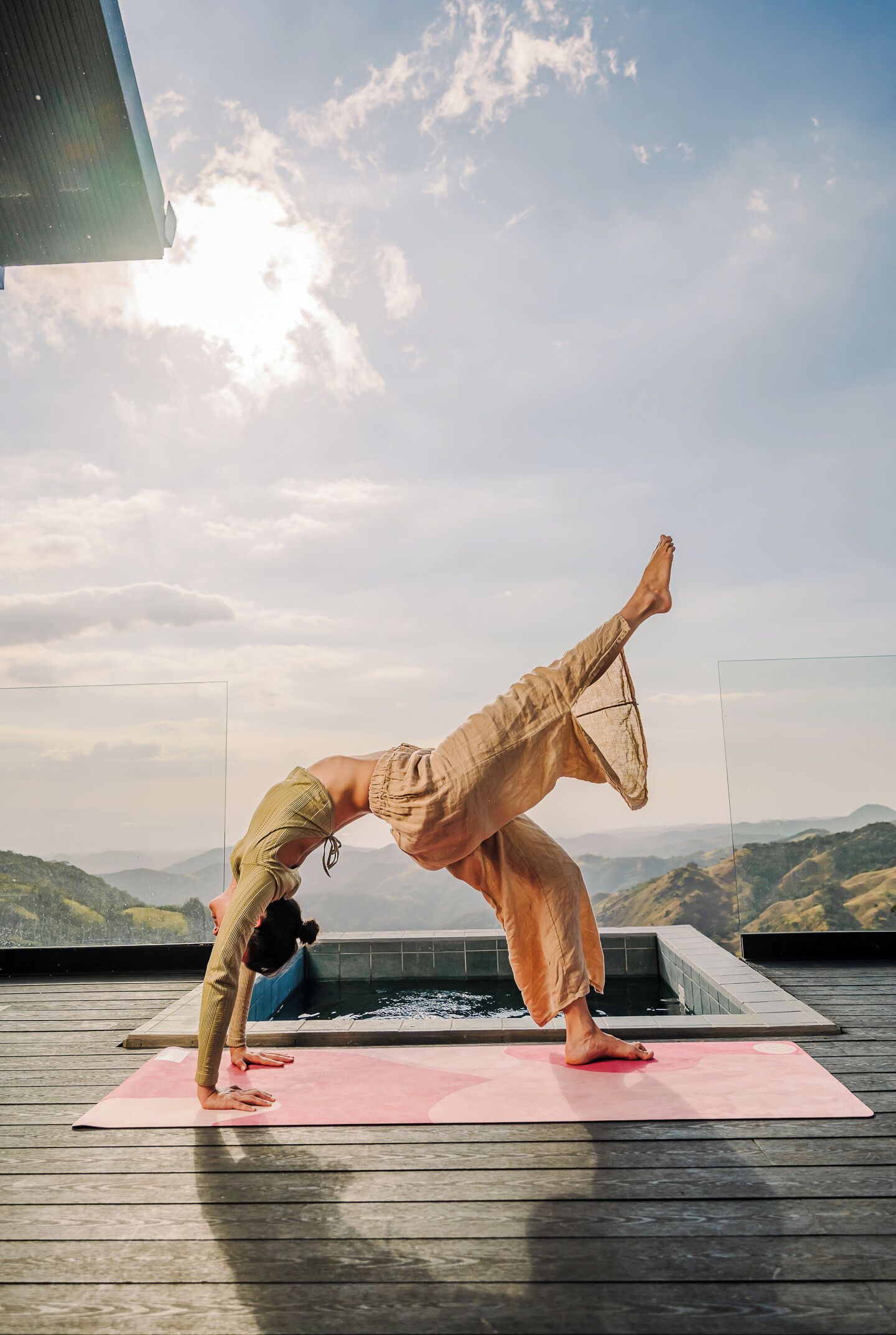 A person performing a yoga pose on a pink mat with a mountainous landscape in the background.