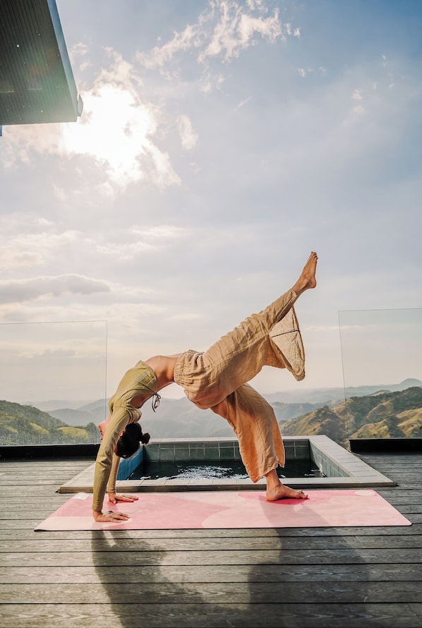 A person performing a yoga pose on a pink mat with a mountainous landscape in the background.