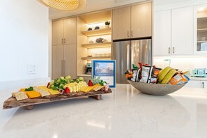 Una cocina moderna con encimera de mármol, una tabla de madera con queso y frutas, y un bol de aperitivos.
