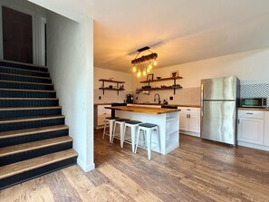 A modern kitchen with a wooden island, white bar stools, a stainless steel refrigerator, and a patterned backsplash. - 2BR/2BA Whitefish Lake Overlook at Suncrest (Whitefish)