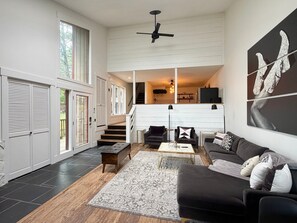 A spacious living area with a black sofa, a coffee table, and a rug. There is a staircase leading to an upper level. - 2BR/2BA Whitefish Lake Overlook at Suncrest (Whitefish)