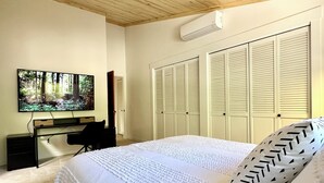 Un dormitori amb un llit, una taula de treball, una cadira, un televisor i un armari.