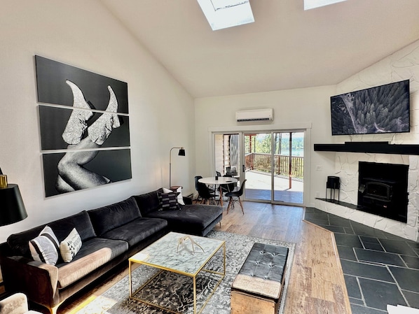 A modern living room with a black leather sofa, a glass coffee table, a fireplace, and a large TV. - 2BR/2BA Whitefish Lake Overlook at Suncrest (Whitefish)