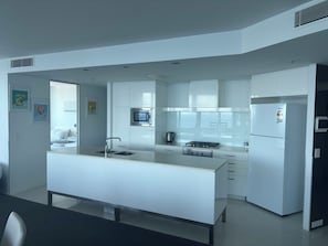 A modern kitchen with white cabinetry, a central island, a microwave, a stove, and a refrigerator. - High Floor Apartment (Surfers Paradise)