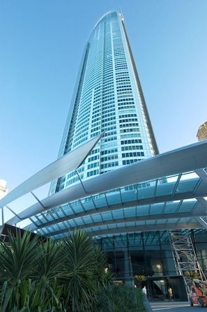 A tall, modern glass building with a curved facade and a covered entrance area. - High Floor Apartment (Surfers Paradise)