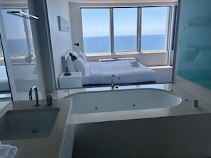 A modern bathroom with a large bathtub, a sink, and a window with a view of the ocean. - High Floor Apartment (Surfers Paradise)