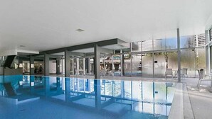 En inomhuspool med väggar av genomskinligt glas, en modern arkitektonisk design och utsikt mot omgivningen.