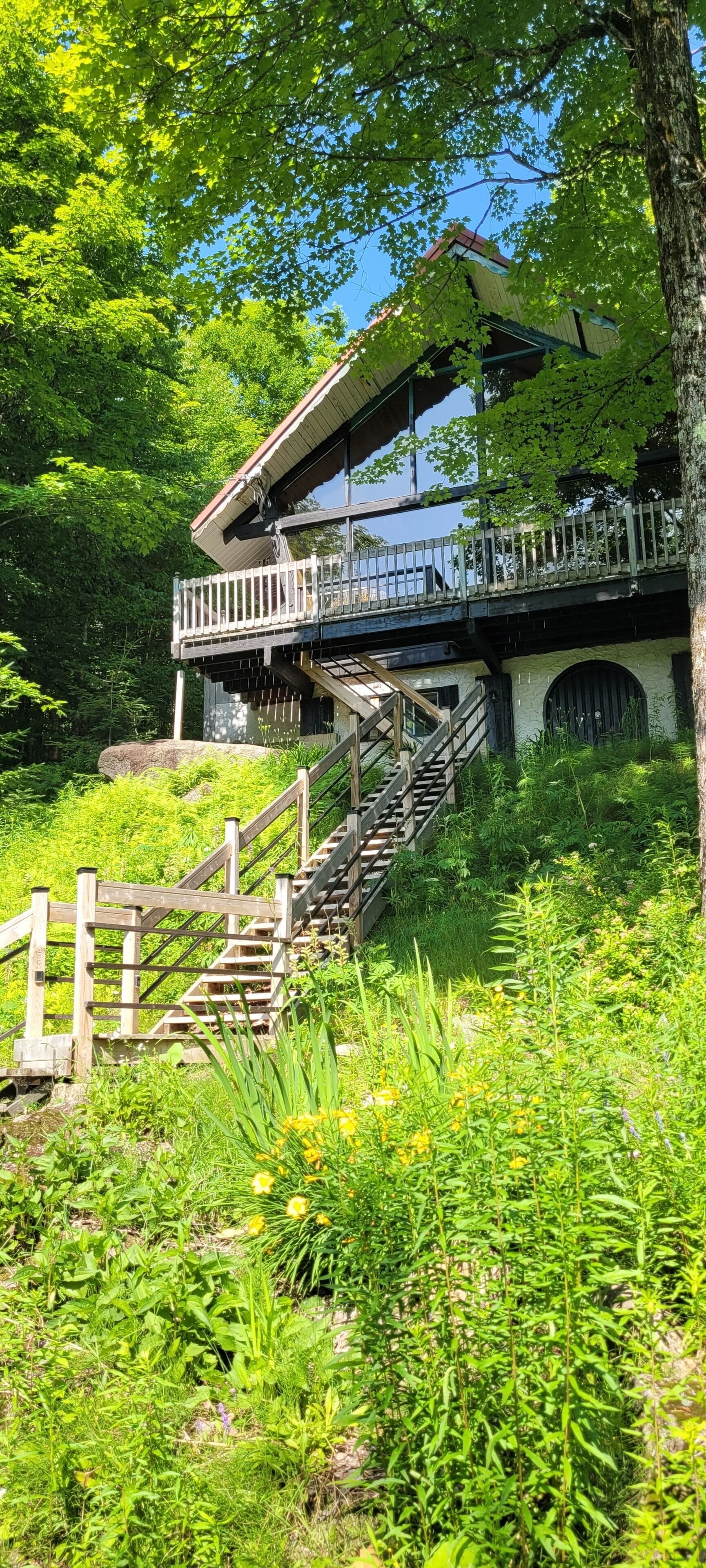 Ein Gebäude mit einer Holztreppe, die zu einem Balkon führt, umgeben von üppigem Grün.