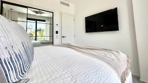 Quarto com cama, televisão fixada na parede e porta para uma varanda.