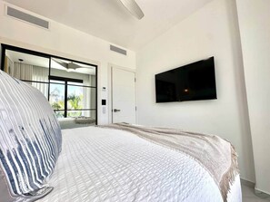 A bedroom with a bed, a TV mounted on the wall, and a door leading to a balcony. - Cana Life Luxury | Cana Rock Universe Pool View (Punta Cana)