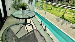 Uma varanda com mesa e cadeiras de vidro, com vista para uma piscina e um gramado bem cuidado.