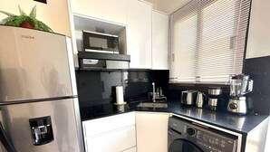Cozinha compacta equipada com geladeira, micro-ondas, fogão e lava-louças.
