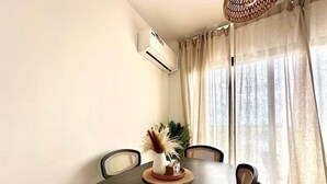 Un coin repas avec une table en bois foncé, quatre chaises, un vase contenant des plantes séchées et un appareil de climatisation fixé au mur.