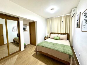 A bedroom with a bed, a nightstand, a mirror, and a sliding door leading to another room. - Cana Life Breeze | Blue Coral Residences C2 (Punta Cana)