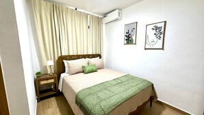 Une chambre à coucher avec un lit, une table de chevet, une lampe, une couverture verte et deux œuvres d’art murales.