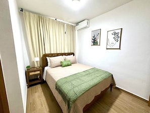 Ein Schlafzimmer mit einem Bett, einem Nachttisch, einer Lampe, einer grünen Decke und zwei Wandbildern.